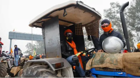 Reuters Farmers sit on a tractor at the frontline of the protest site as they march towards New Delhi to press for better crop prices promised to them in 2021, at Shambhu barrier, a border crossing between Punjab and Haryana states, India, February 21, 202