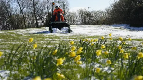 PA Media A council worker mows a lawn that has been dusted with a light covering of snow in Beamish, Durham