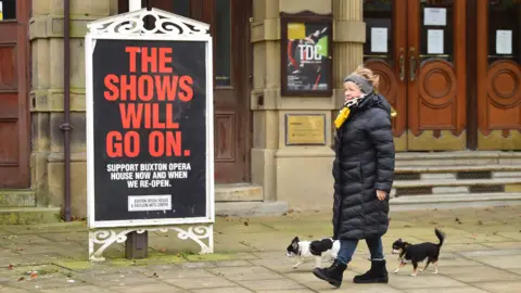 Getty Images Woman walking past a theatre sign saying "The shows will go on"