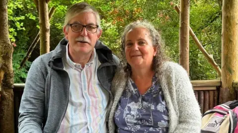A couple in their 60s sat smiling at the camera.
