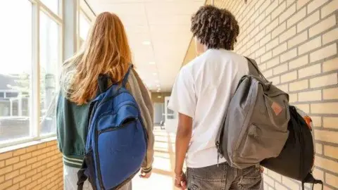 Two students - a young woman and a young man - carrying backpacks along a corridor