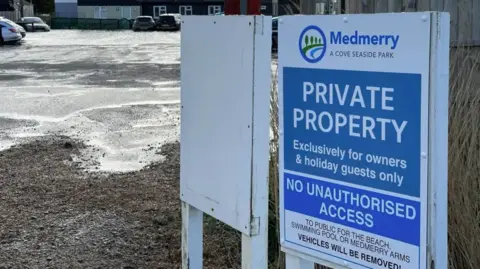 Sophia Cobby/BBC A sign that says private property and shows a flooded car park behind with cars in it