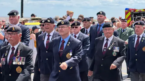 Dale Baxter/BBC A close up photo of veterans marching through the parade in their uniforms. The gentlemen wear berets and their medals with a shirt and tie and jackets with emblems.