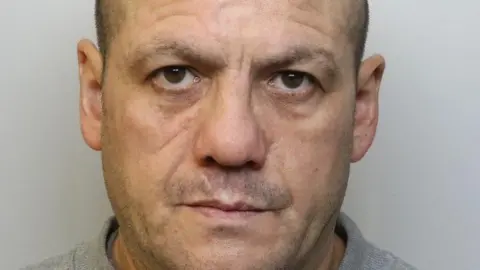 Avon and Somerset Police A mugshot of Wayne Milsom. He has short dark hair and is wearing a grey jumper.