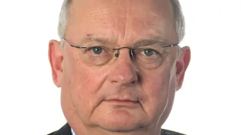 Suffolk County Council A close-up headshot of Andrew Reid, who is wearing glasses and staring into the camera. 