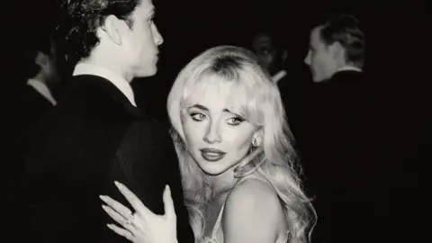 Black and white image of Sabrina Carpenter holding a man's arm