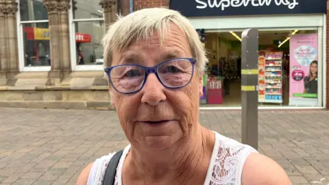 Steve Jones/BBC Janet Towler, who has short grey hair and blue-rimmed glasses. She is looking directly at the camera in the headshot.