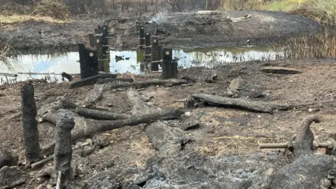 A low angle shot of a bridge devastated by a fire where the fixtures are the only parts still standing, the rest is burnt black