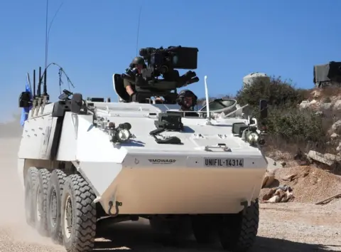 Irish Defence Forces Two Irish peacekeepers driving a white tank down a sandy road in Lebanon