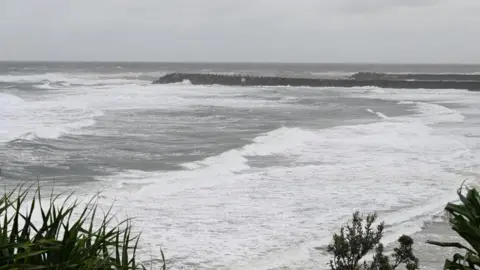 A rocky pier extends into rough seas