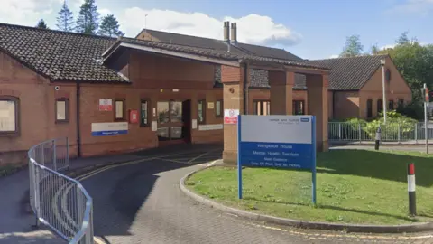 The entrance to Wedgwood House. A brown-bricked building with an NHS blue and white sign outside. 