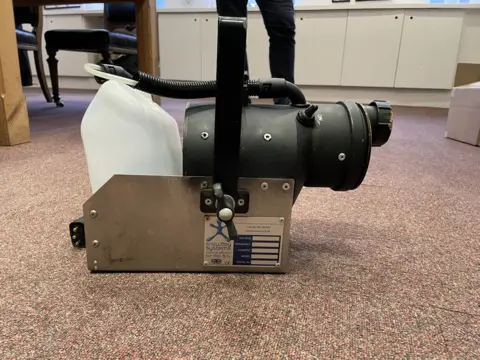 Health and Safety Executive A mechanical snow machine sitting on a carpet. It comprises of a stainless steel box with black and plastic components. 
