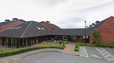 Google A general view of a care home. There are outdoor chairs and tables sat outside the home. There are disabled car parking spaces outside the home. 