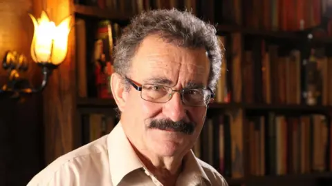 Professor Robert Winston faces the camera in a library.