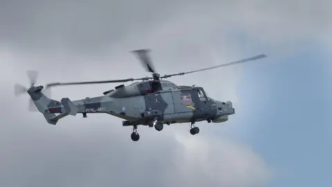 A UK military helicopter in flight. It has battleship grey camouflage.