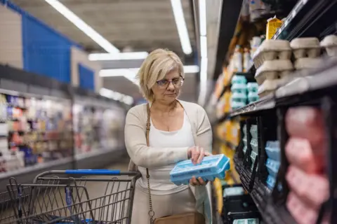 Getty Images A woman examines a carton of eggs in a grocery store