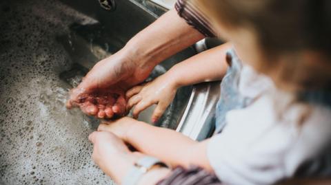 An adult and child wash their hands in soapy water