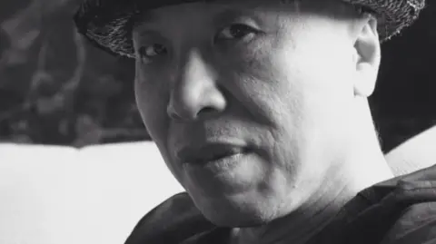 Black and white image of Gao Zhen wearing a hat and looking at the camera