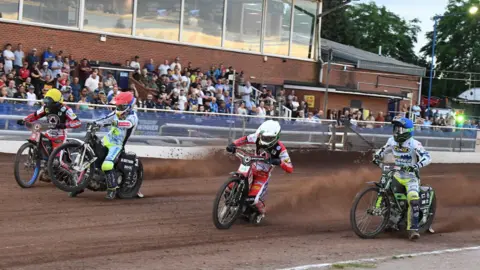 Ian Wagstaff Four speedway riders race around the track as the Oxford crowd watches on.