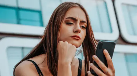 Photograph of young woman looking at mobile phone with serious expression on her face.
