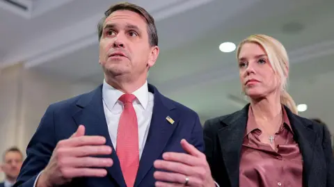 Getty Images Todd Blanche and Pam Bondi speak with the media in the Capitol in March 2026. Blanche is wearing a blue suit and red tie, while Bondi is wearing a pink shirt and a black jacket 