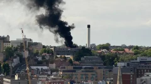 A skyline shot of Bristol showing the fire at St Michael's Hospital. A thick black smoke plume can be seen coming from the roof of the building. The Cotham area of the city can be seen in the distance.