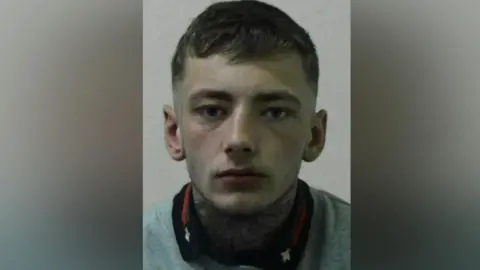 Mugshot of a man with short dark hair and a large spider web tattooed across the front of his neck