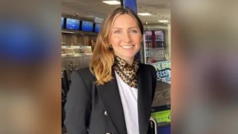 Cherise Abbott Cherise Abbott looking and smiling directly at the camera. She is wearing a white T-shirt and black blazer and a leopard print scarf.