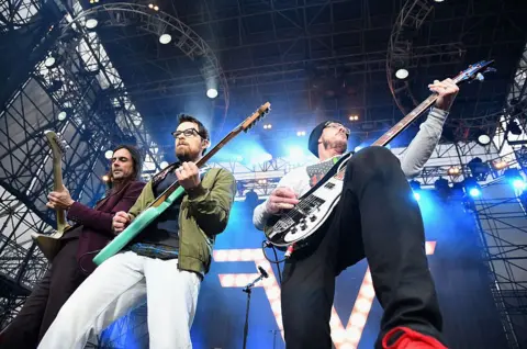 Getty Images Weezer are shot from below as they perform on a vast stage surrounded by scaffolding