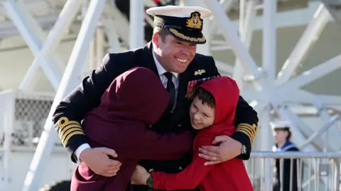 PA Media Captain Richard Hewitt, commanding officer of HMS Prince of Wales, is greeted by his sons Oliver and William