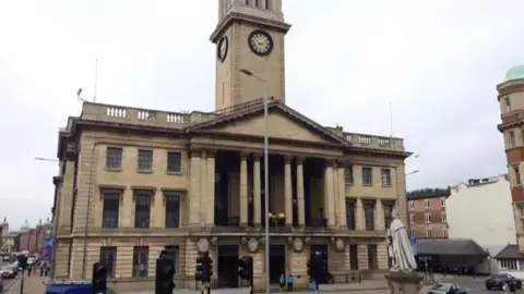 BBC The Hull Guildhall. It is a three-storey light stone building with columns on the front and a clock tower in the middle.