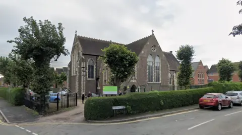 A stone church building surrounded by trees and hedgerows