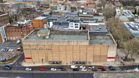 Peterborough from Above Drone image view of a derelict multi-storey building with the Bourges Boulevard adjacent to it. There are other buildings behind it.