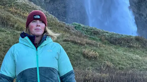 Runclub Sarah Meenan stands in the countryside in north Wales. She is wearing hiking gear and a woolly hat and looking away from the camera, inspired by the landscape.
