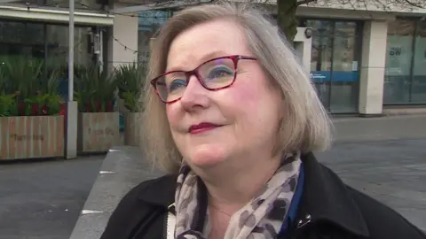 Lorna is wearing glasses, a dark coat and a brown scarf