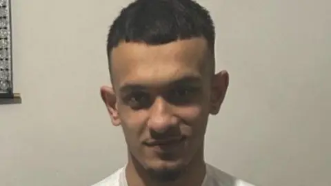 South Yorkshire Police Hamza Mohammed. A man with a thin brown face and short black hair looks at the camera with a slight smile. The neck line of a white top is showing.