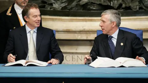 Getty Images Tony Blair dan Jack Straw duduk di meja dengan buku besar di depan mereka dan mereka memegang pena.