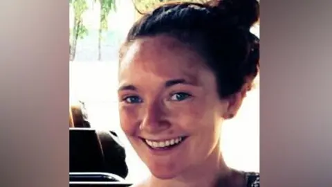 PA Media Danielle McLaughlin smiling at the camera.  She has long auburn hair tied up in a bun.  She is wearing a dark, patterned top.