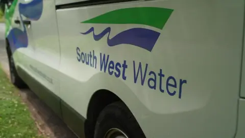 The side of a white van parked on the side of the road. The South West Water logo is on the door of the van with blue and green streaks.