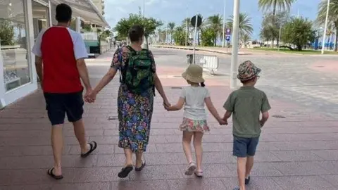 Family handout A man in a red and white t-shirt holds hands with a woman wearing a flowery dress, a girl and a boy as they walk down a street with palm trees in the background. All of them have their backs to the camera.