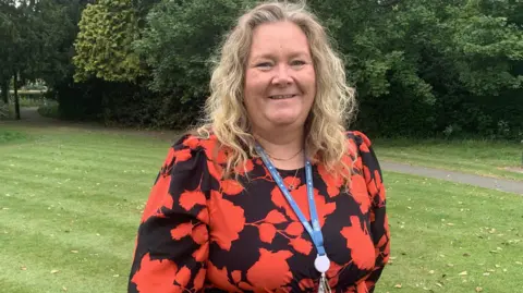 North Yorkshire Council A woman with blonde hair standing on a grass lawn wearing a red and black floral dress