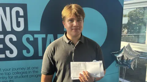 A student holds up his sheet of results to the camera on results day.