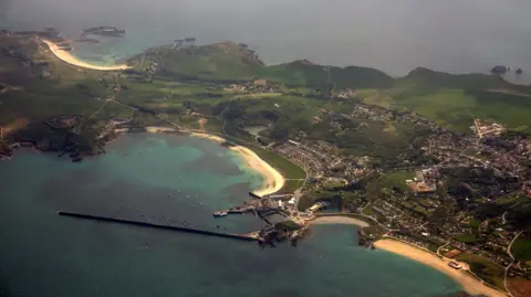 BBC An aerial view of Alderney showing a harbour, housing and green fields. 