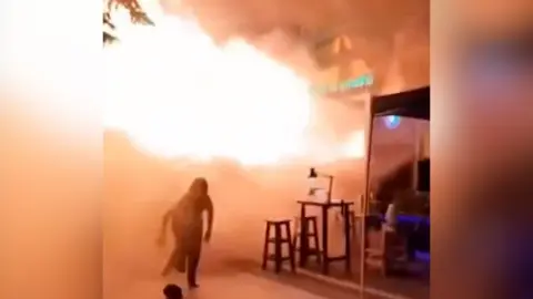 Someone runs from flames erupting from a bar doorway