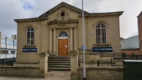 The outside of the Wesleyan Reformed Church building, a stone-brick building. The building has steps leading up to double wooden doors.