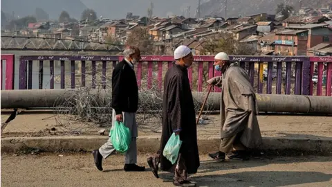 Getty Images Elderly men walk over a bridge on a cold winter day as residential houses are seen in the background in Baramulla Jammu and Kashmir India on 25 November 2022