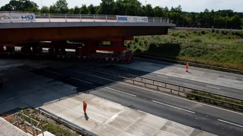 PA Media HS2 workers watch as a bridge is wheeled into position over the M42