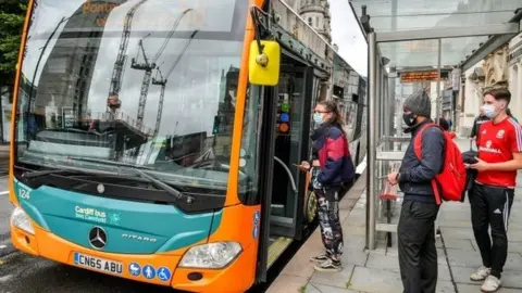 PA Media Passengers in masks getting on a bus in Cardiff