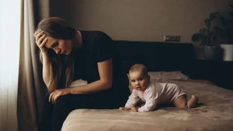 Getty Images Woman sitting on bed with a baby