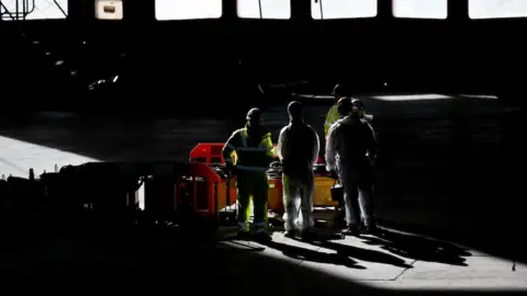 ©JMP UK/Ashley Crowden Workmen stand in a shaft of sunlight inside the Brabazon Hanger that will become Bristol's concert arena